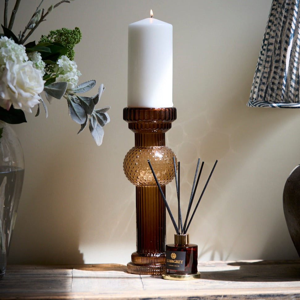 Pillar candle statement in amber sitting on a side board with a reed diffuser
